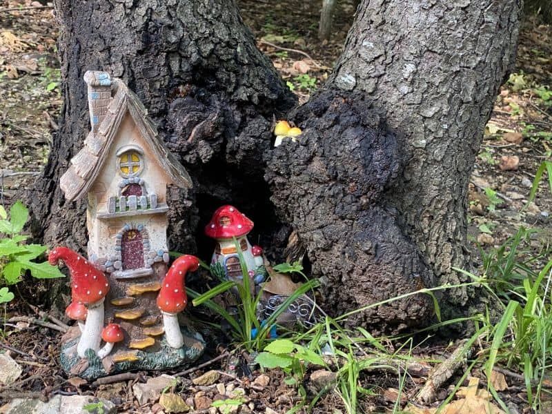 A fairy house is sitting next to a tree in the woods.