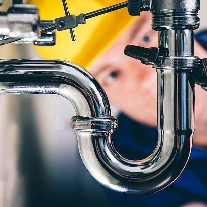 Plumber in hard hat inspecting chrome plumbing under a sink.