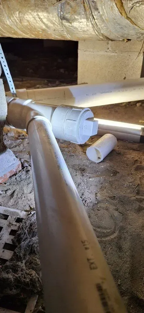 PVC pipes in a crawlspace; some are cut and lying on the ground.