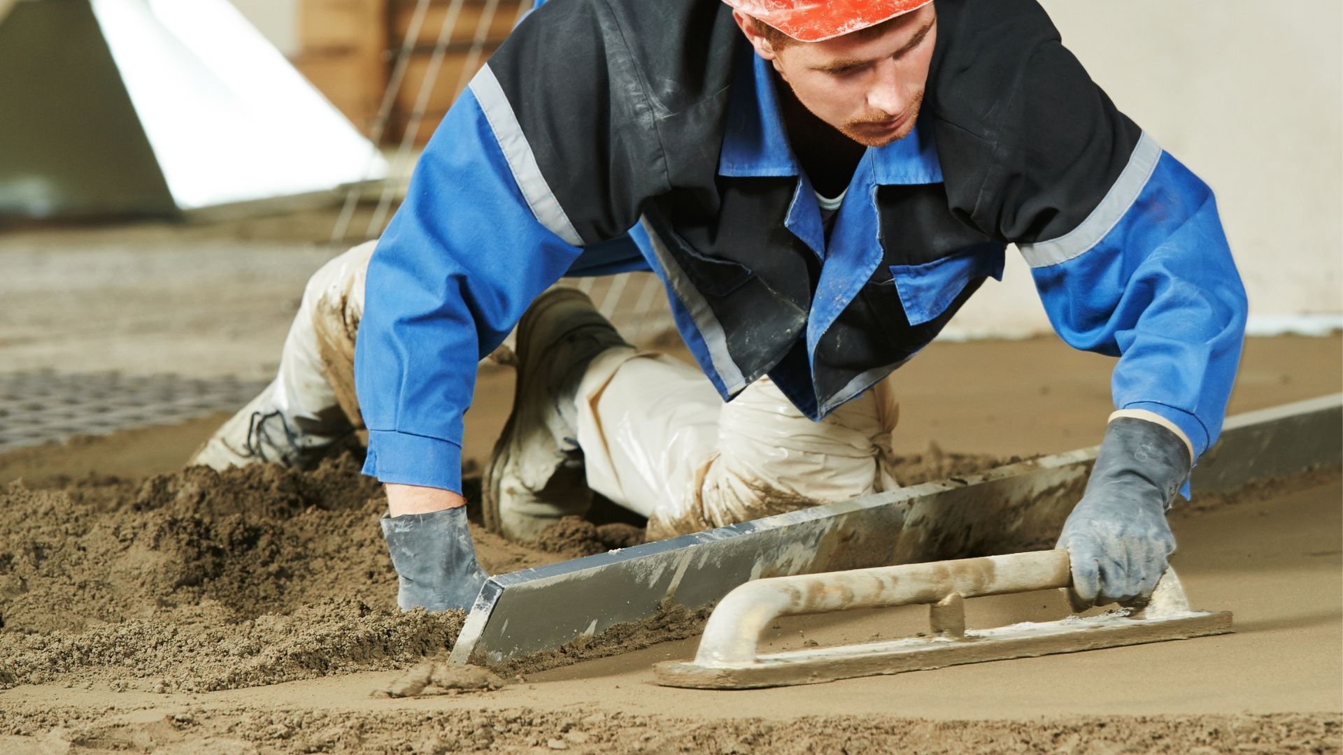 A man is laying concrete on the ground with a trowel.
