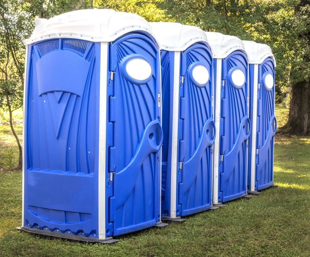 A Row of Blue Portable Toilets Are Lined Up in a Grassy Field — AM & JD Contracting In Muswellbrook, NSW