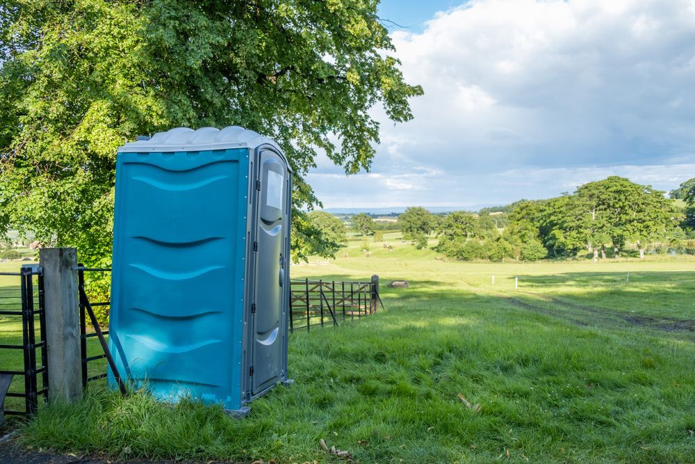A Blue Portable Toilet is Sitting in the Middle of a Grassy Field — AM & JD Contracting In Muswellbrook, NSW