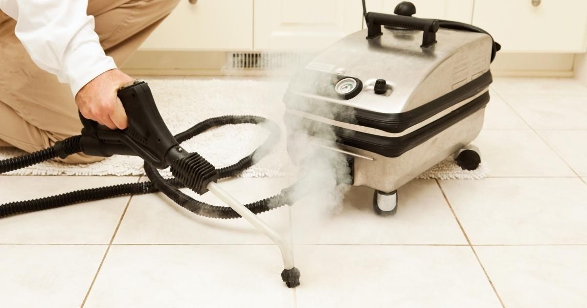 Person steam cleaning tile floor with a steam cleaner, spraying steam.