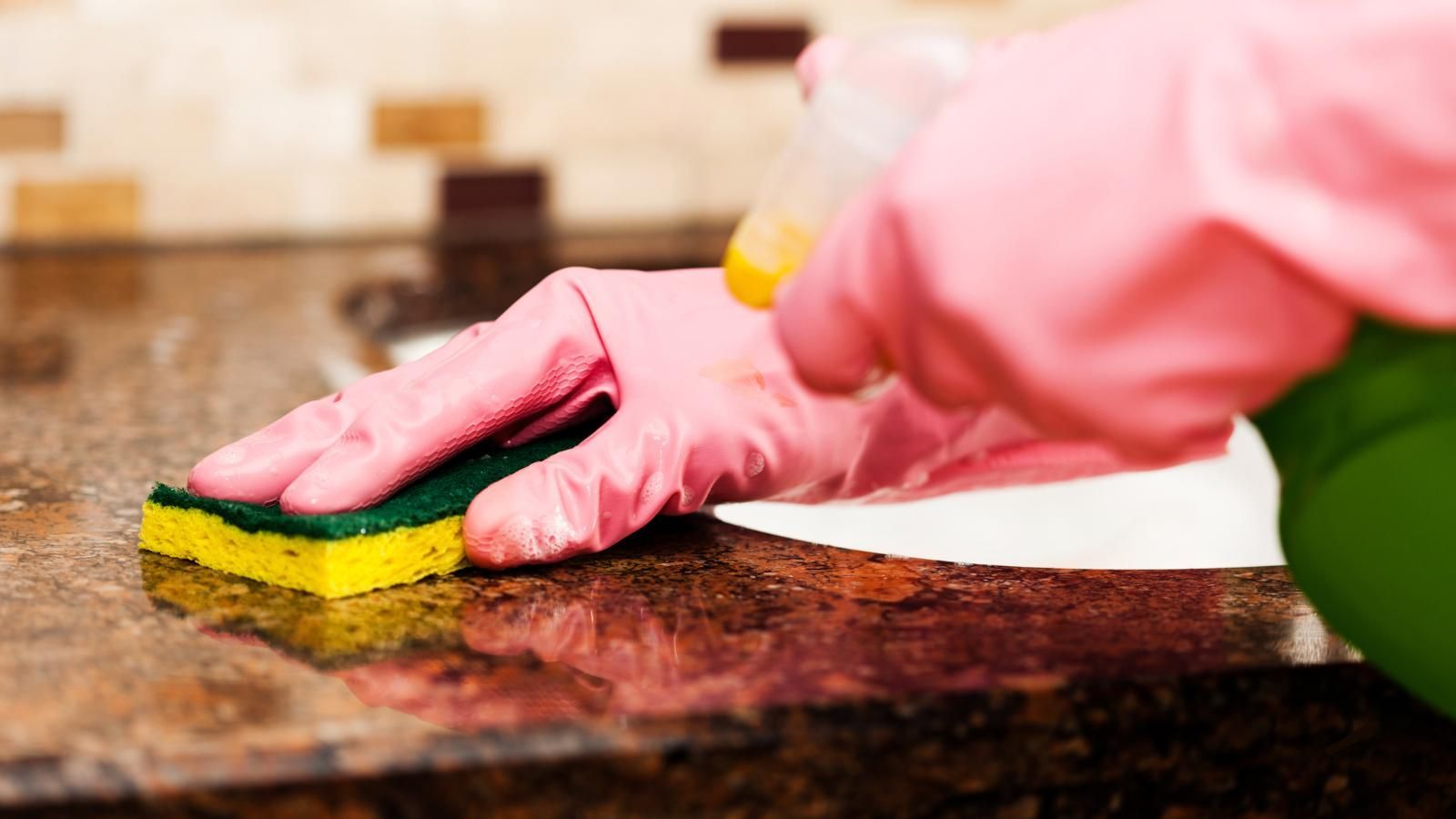 Gloved hand wiping down granite countertop with sponge.