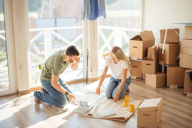 A man and a woman are kneeling on the floor in a room with cardboard boxes.