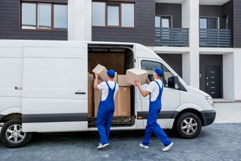 Two movers are loading boxes into a van in front of a house.