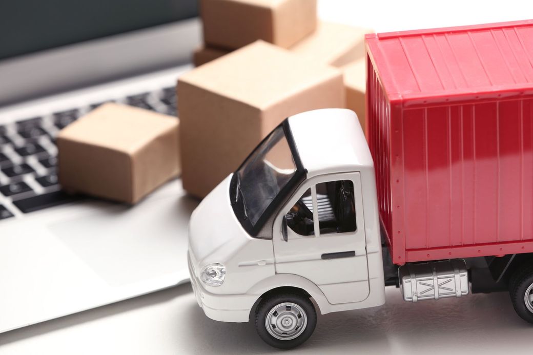 A toy truck is parked next to a laptop and boxes.