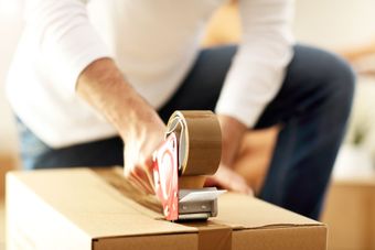 A man is taping a cardboard box with brown tape.