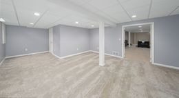 Empty carpeted basement room with gray walls, white columns, and recessed lighting