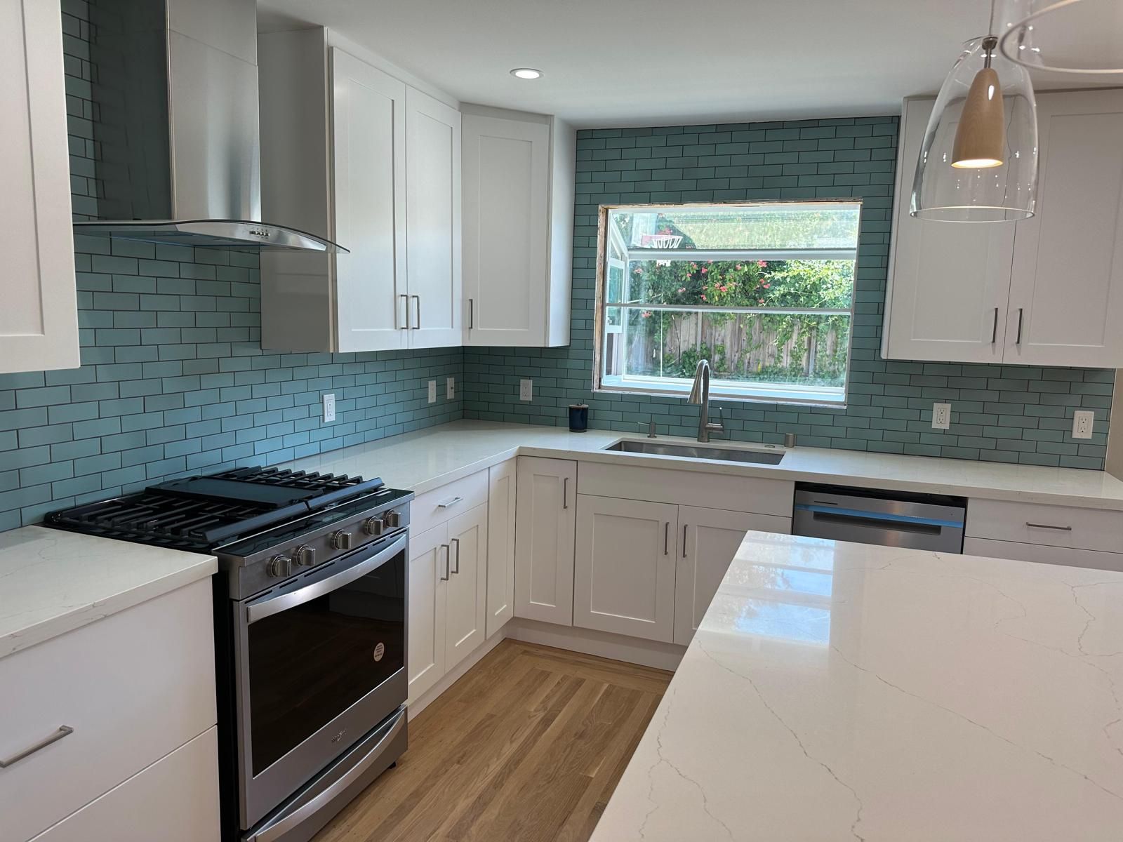 A kitchen with white cabinets , a stove , a sink , and a window.