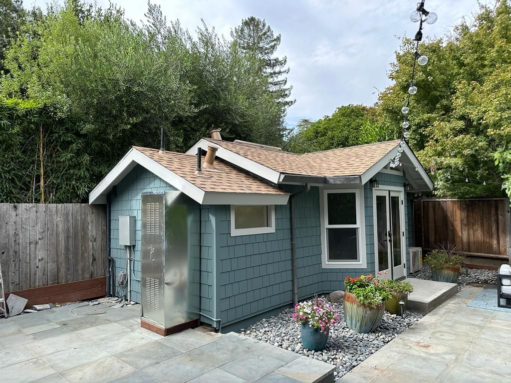 A small blue shed with a brown roof is in a backyard surrounded by trees.