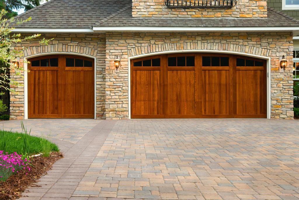 A stone house with wooden garage doors and a brick driveway