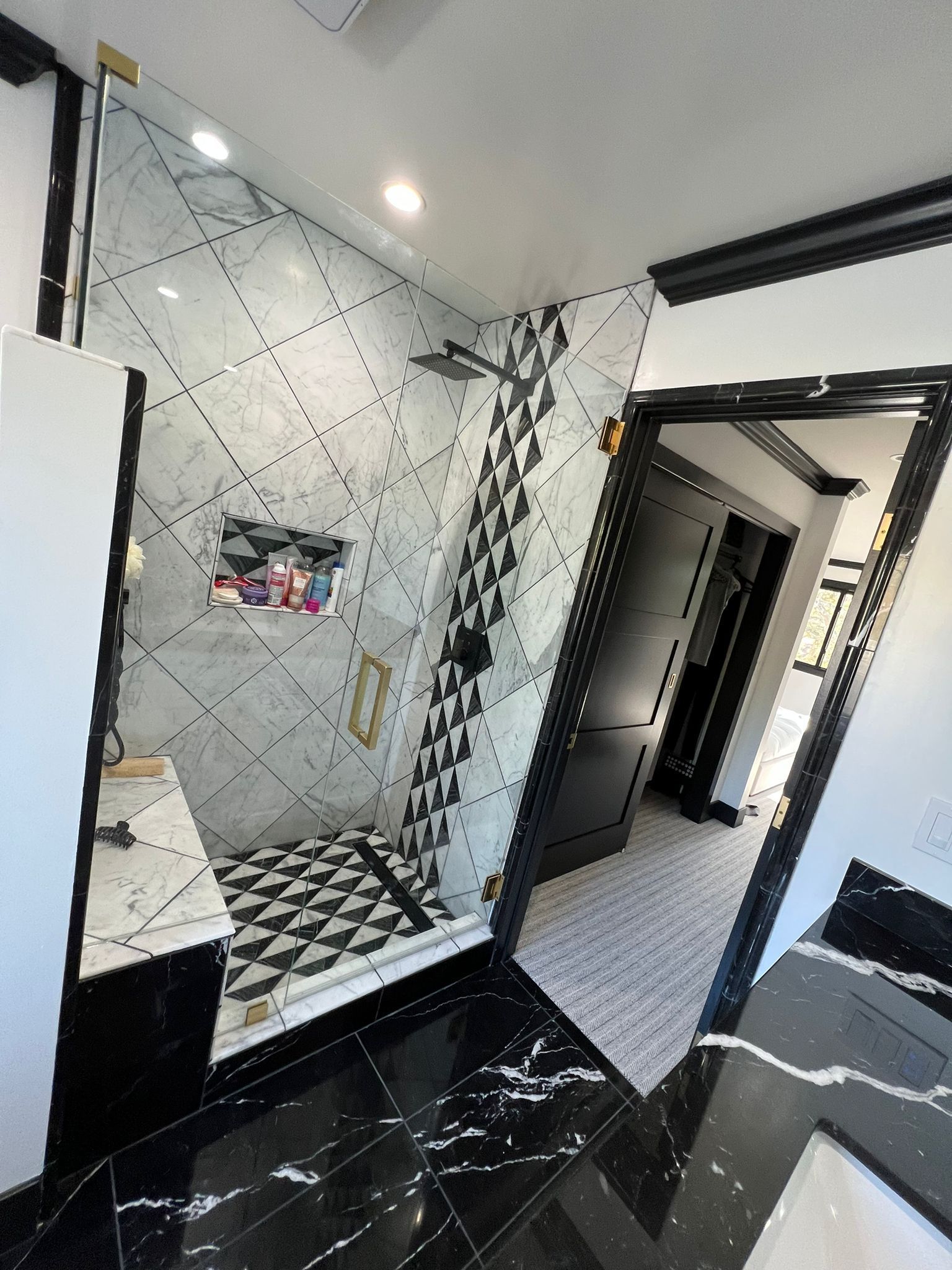 A bathroom with a walk in shower and black and white tiles.