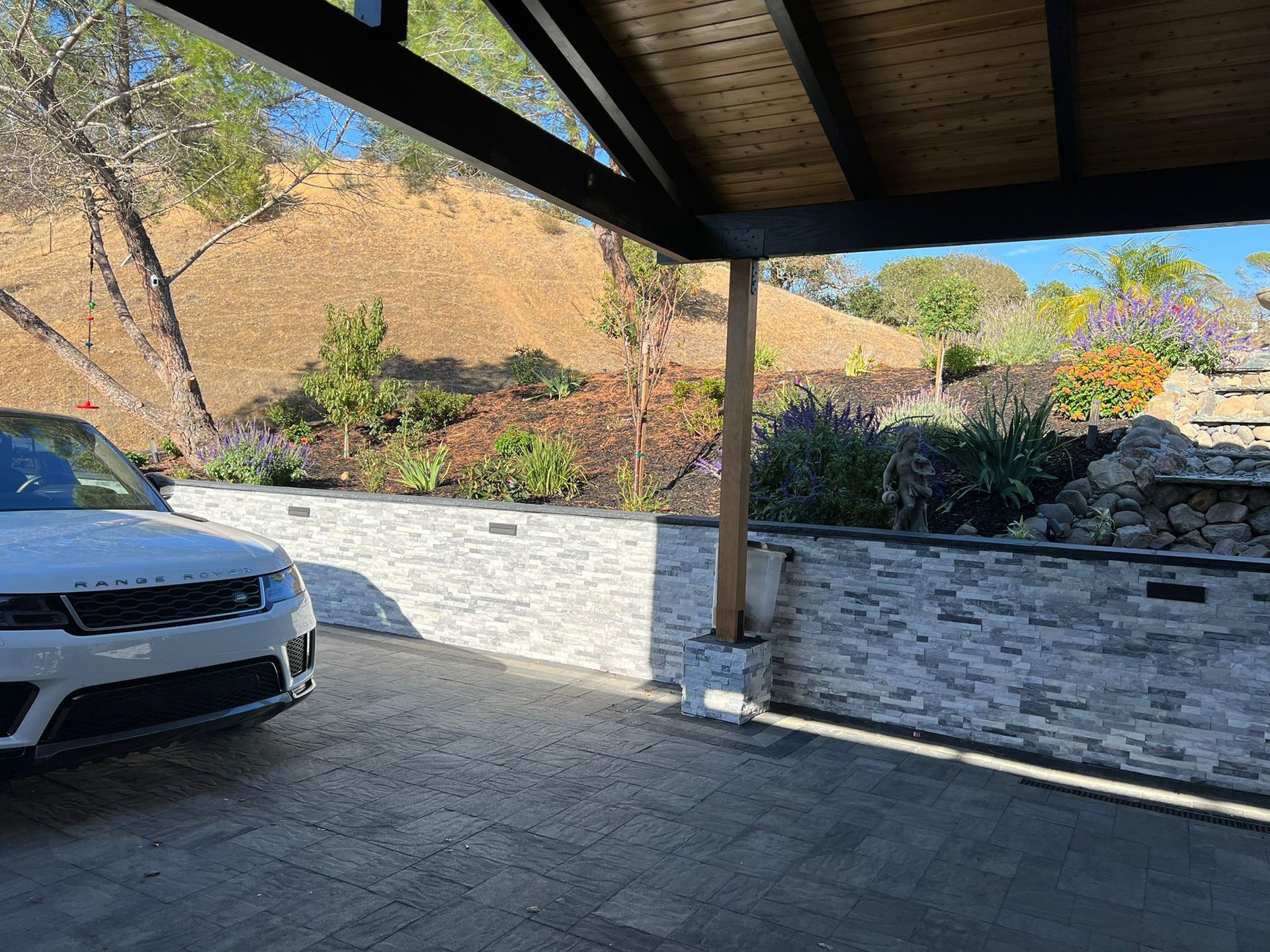 A white car is parked under a canopy in a driveway.