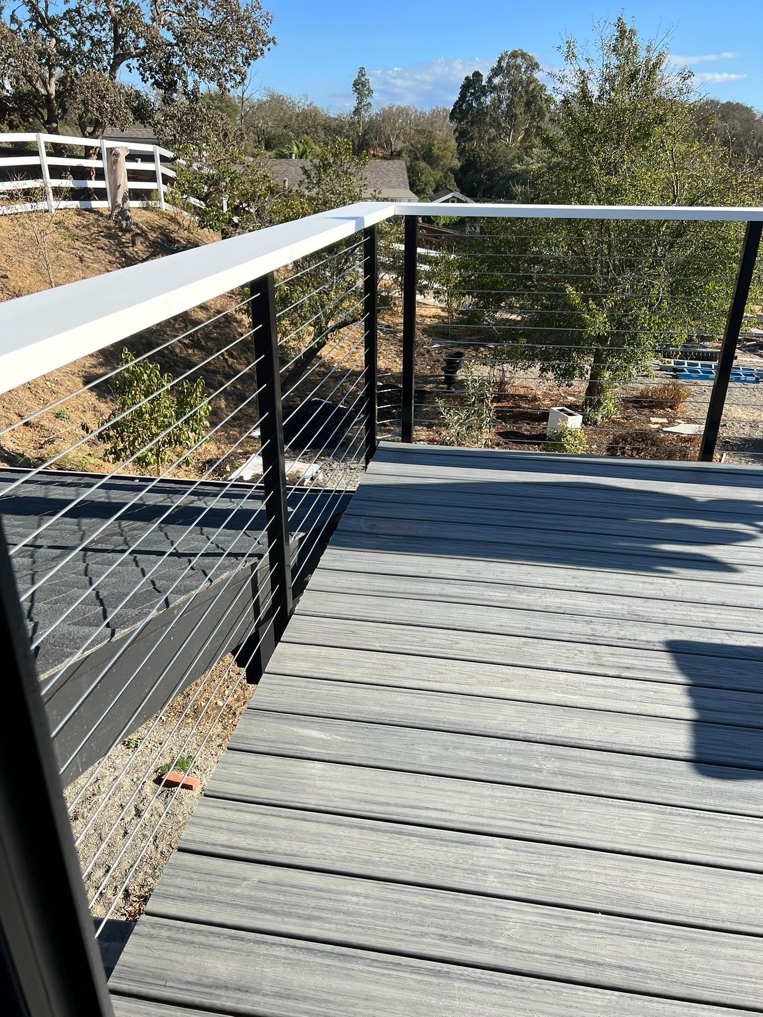 A gray deck with a black railing and a view of trees.