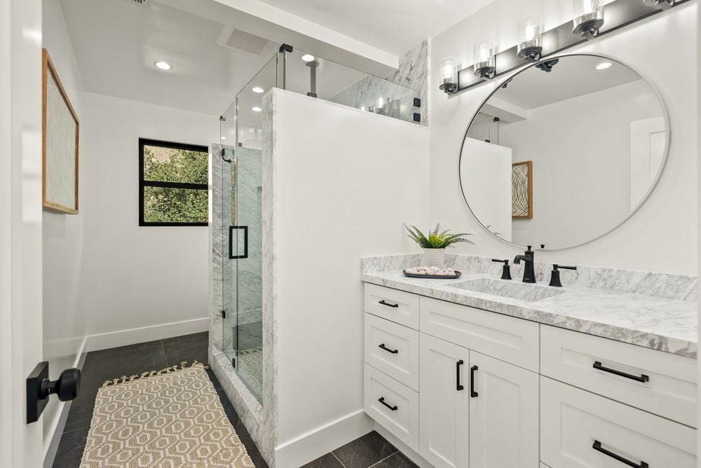A bathroom with a sink , mirror and walk in shower.