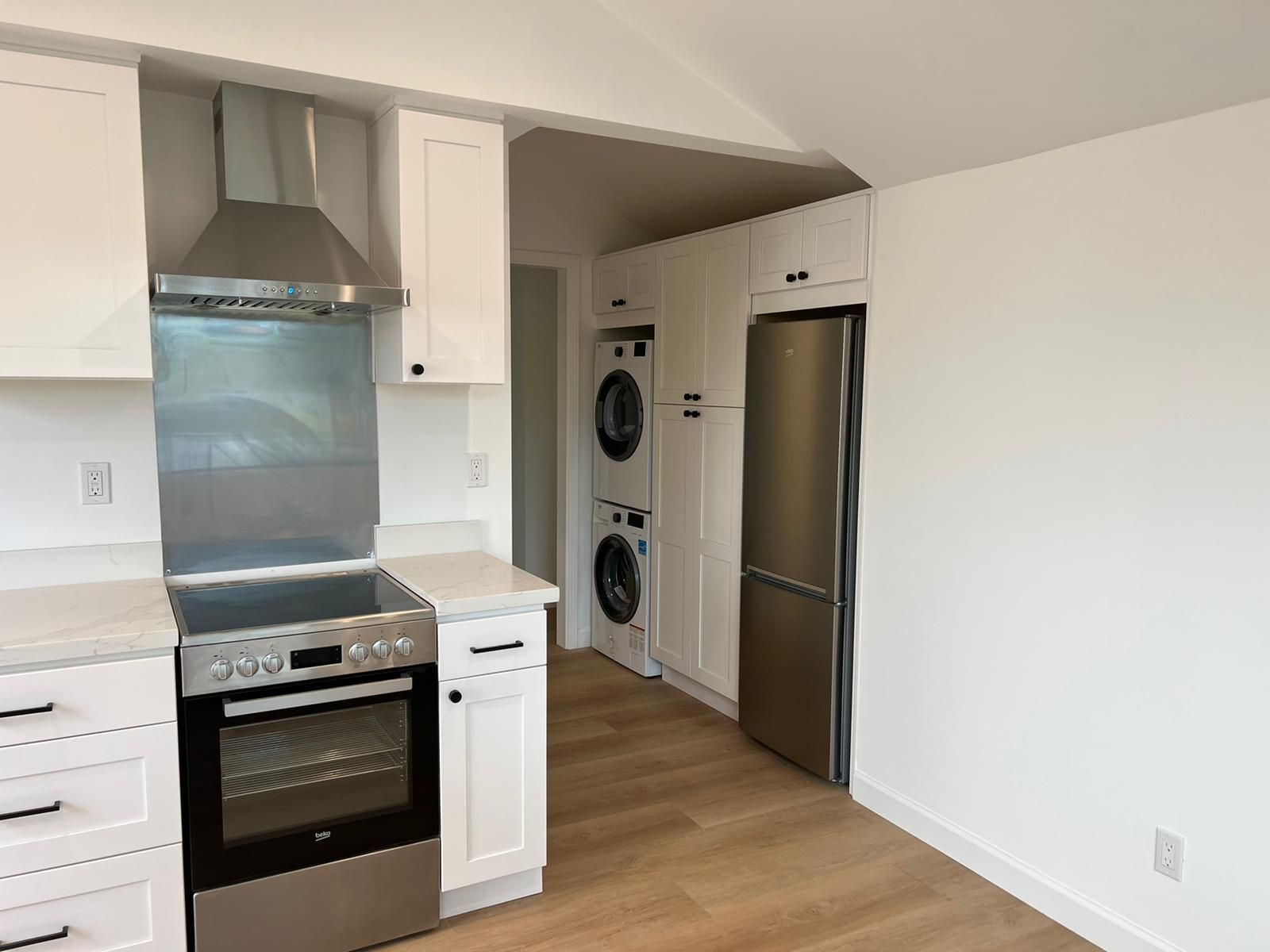 A kitchen with a stove , refrigerator , washer and dryer stacked on top of each other.