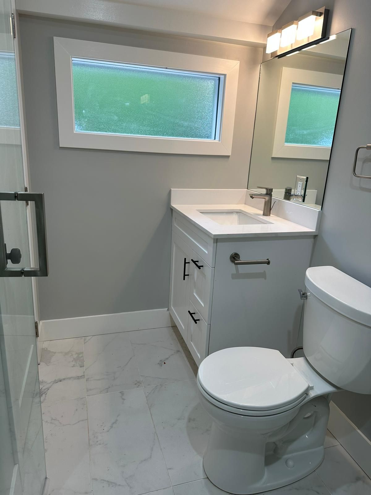 A bathroom with a toilet , sink , mirror and window.