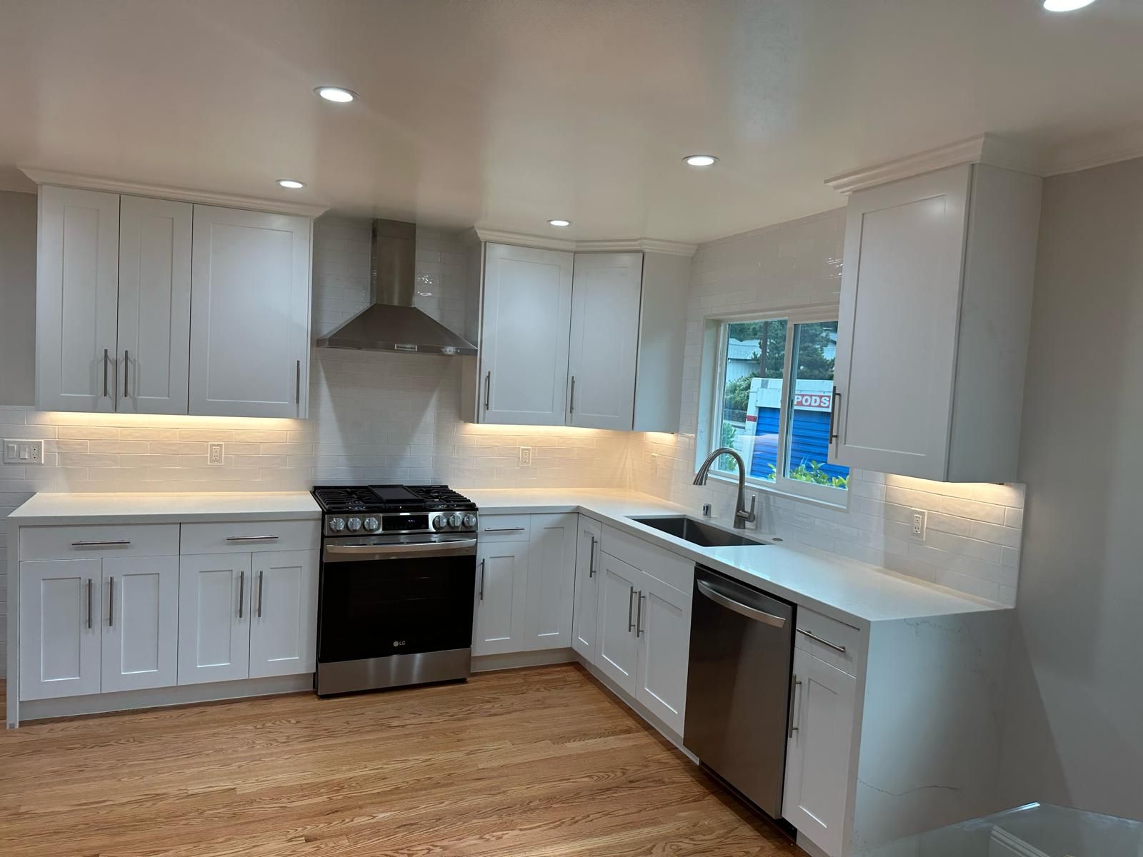 A kitchen with white cabinets , a stove , a sink , and a window.