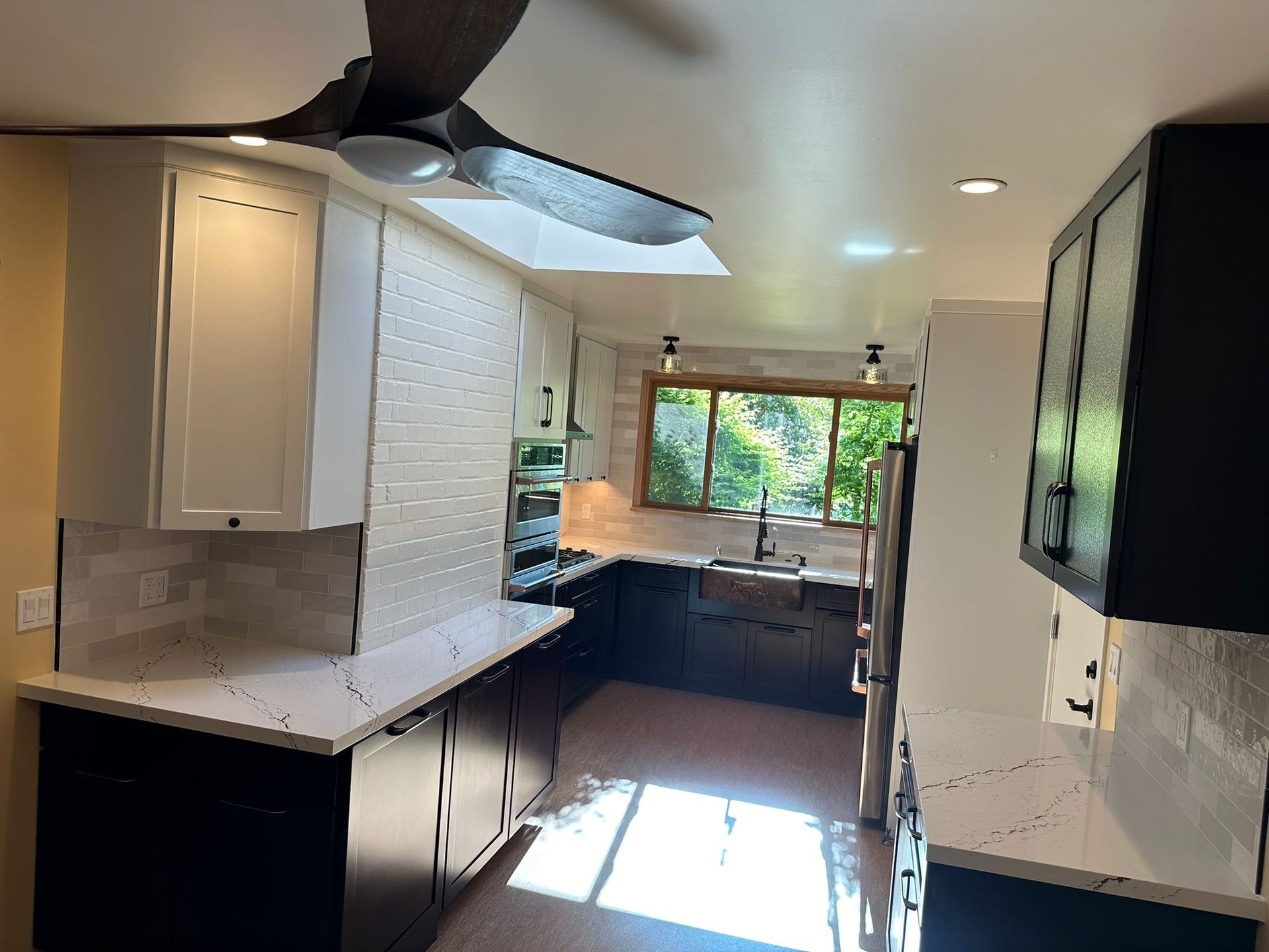 A kitchen with black cabinets and white counter tops and a ceiling fan.