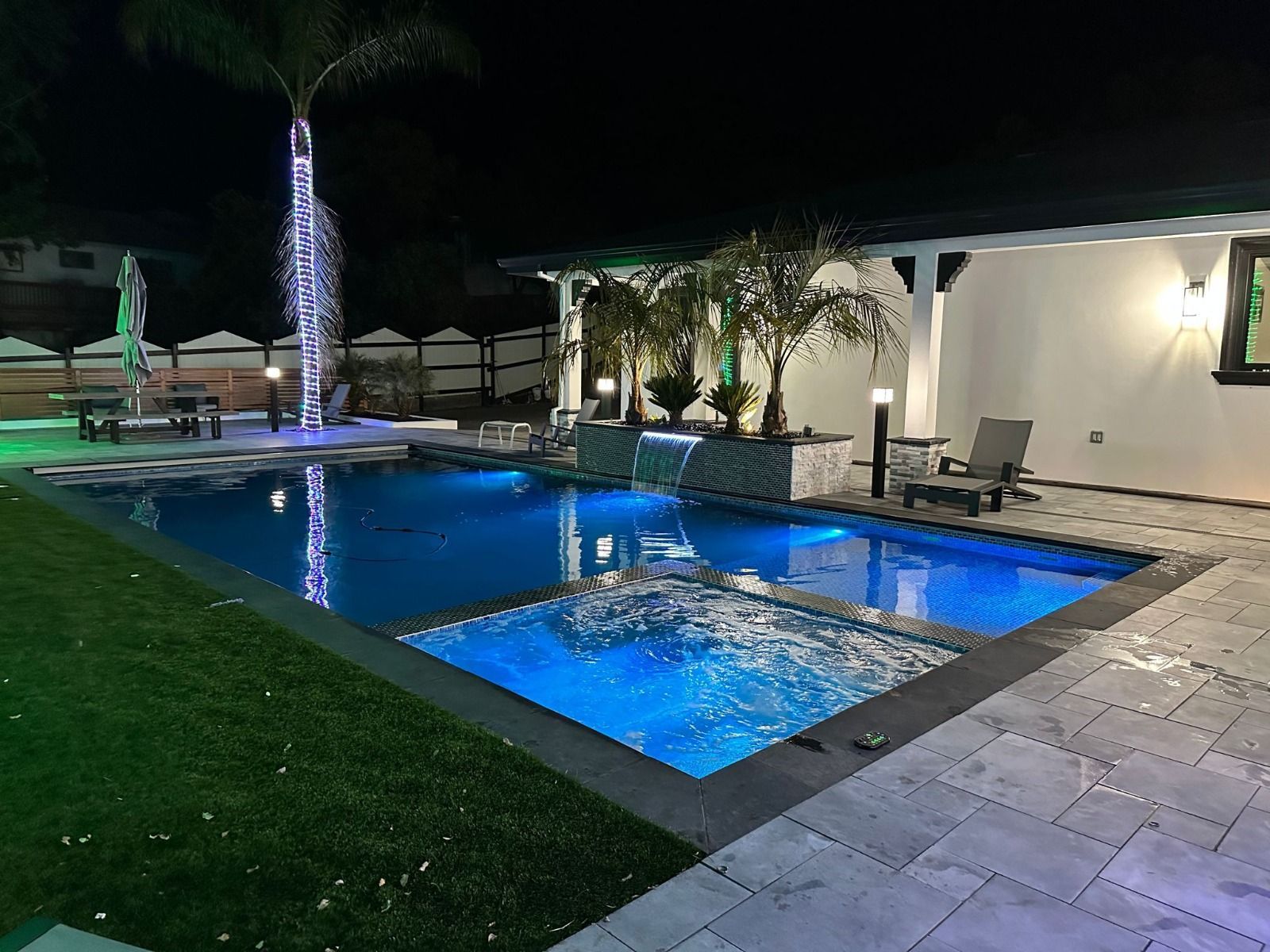 A large swimming pool is lit up at night in a backyard.