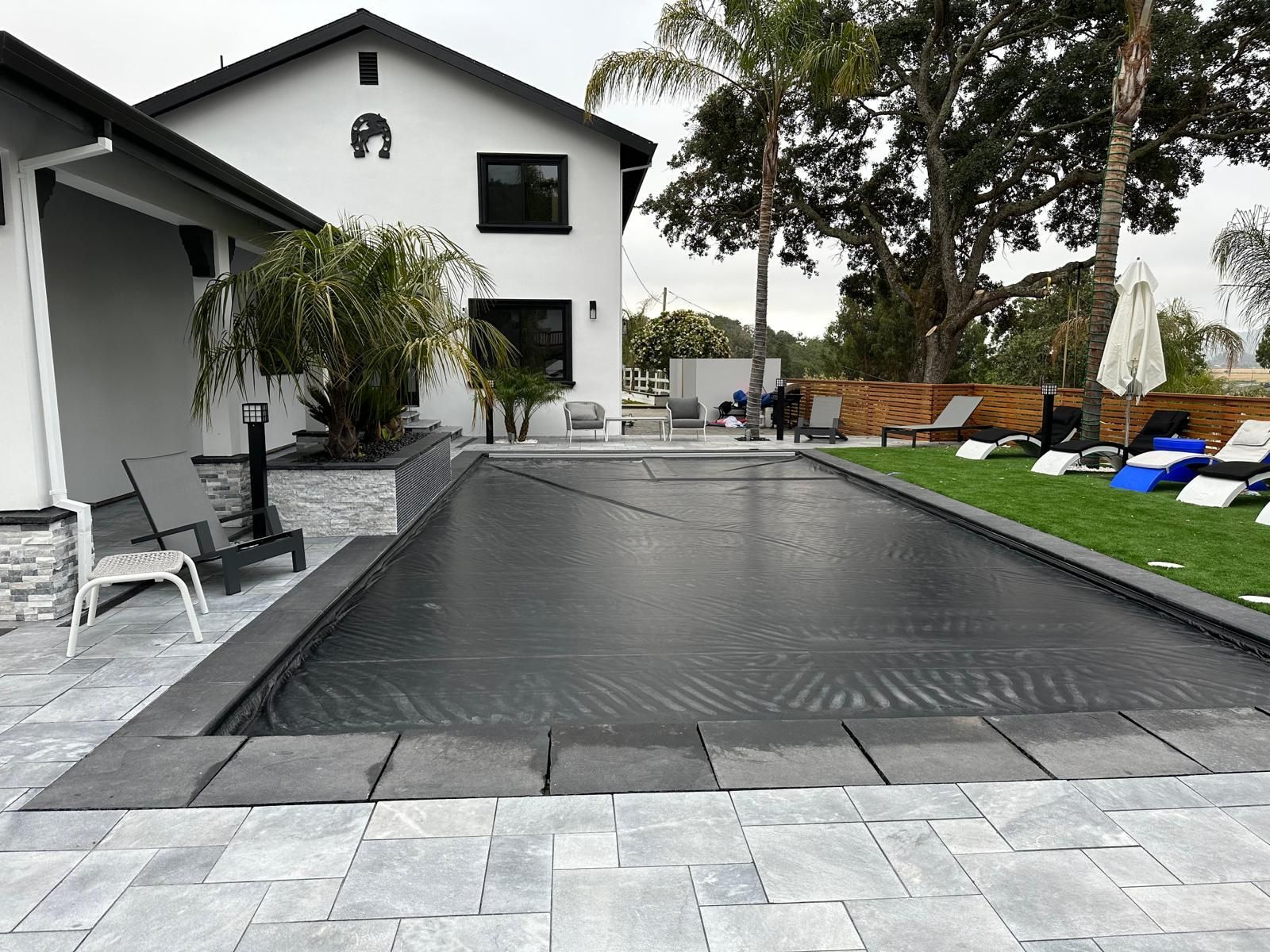 A large swimming pool is surrounded by chairs and umbrellas in front of a house.