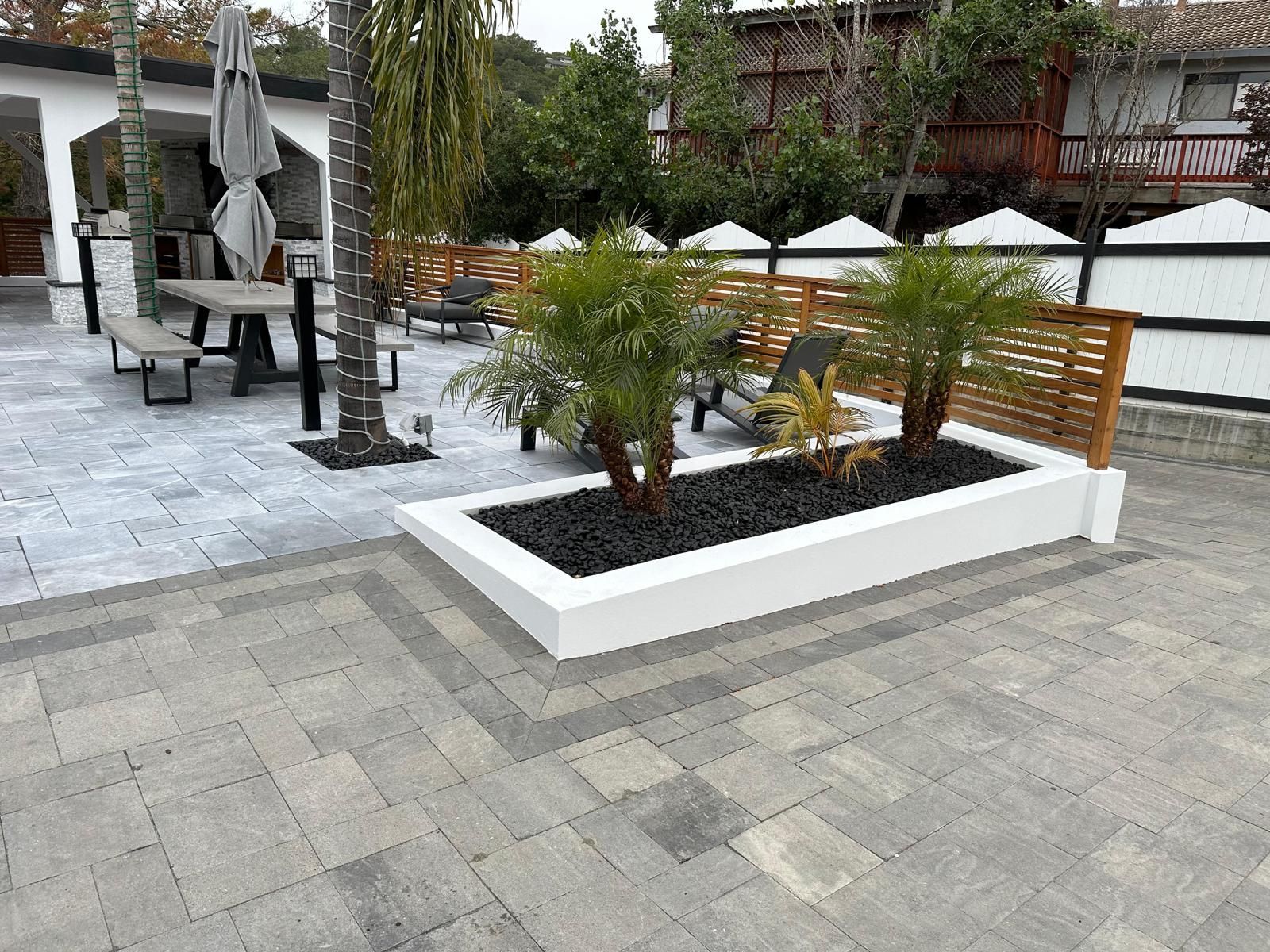 A patio with a white planter filled with plants and chairs.