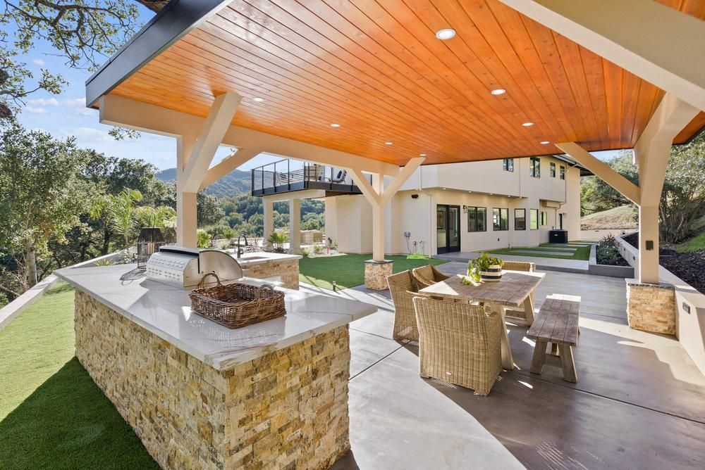 A patio with a table and chairs under a wooden roof.