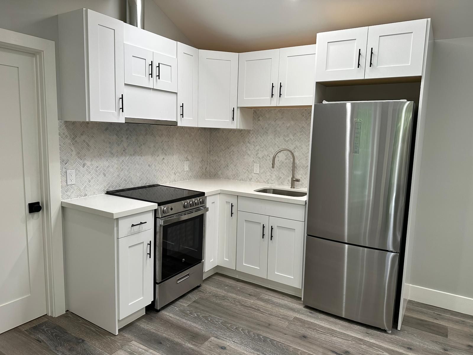 A kitchen with white cabinets , a stove , a refrigerator , and a sink.