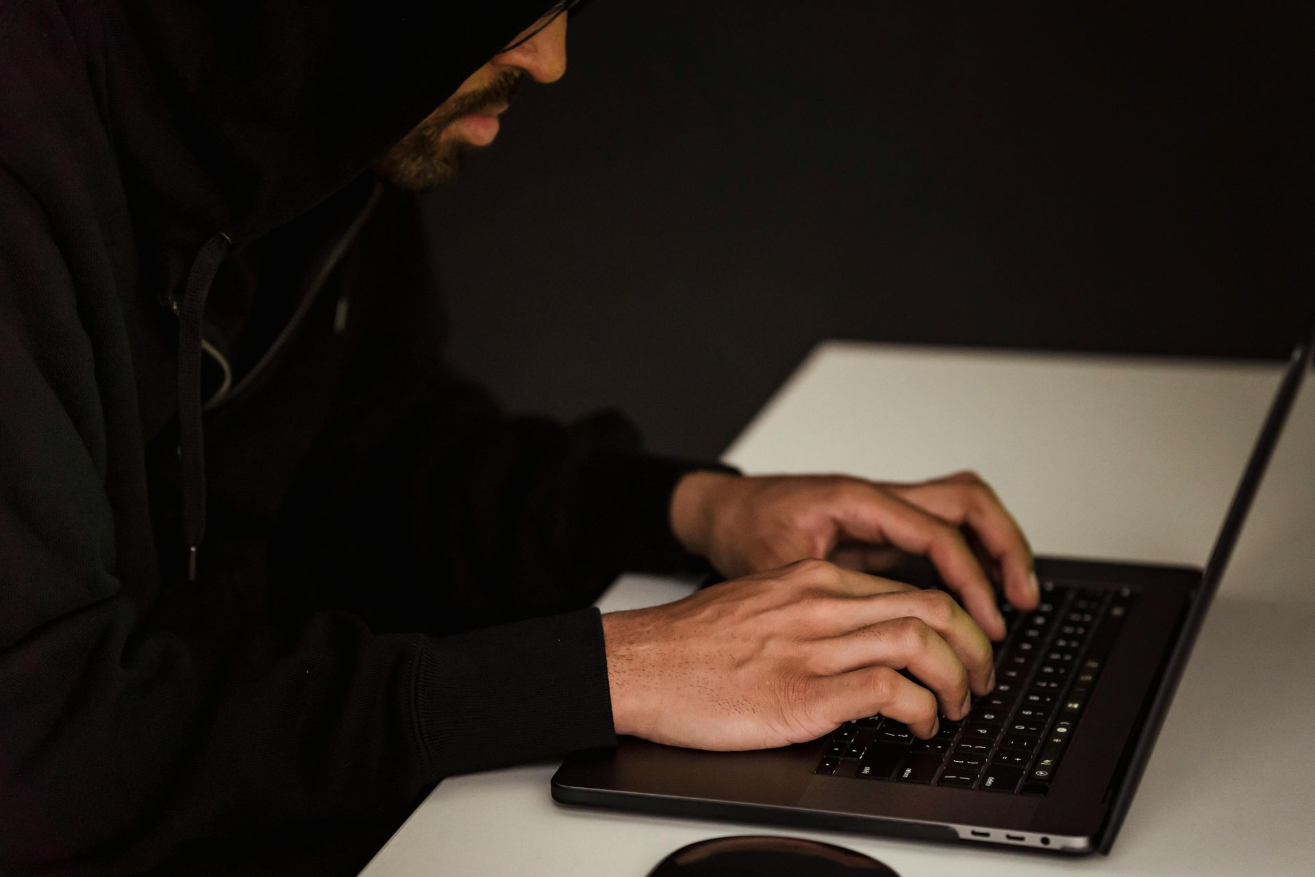 A man in a hood is typing on a laptop computer.