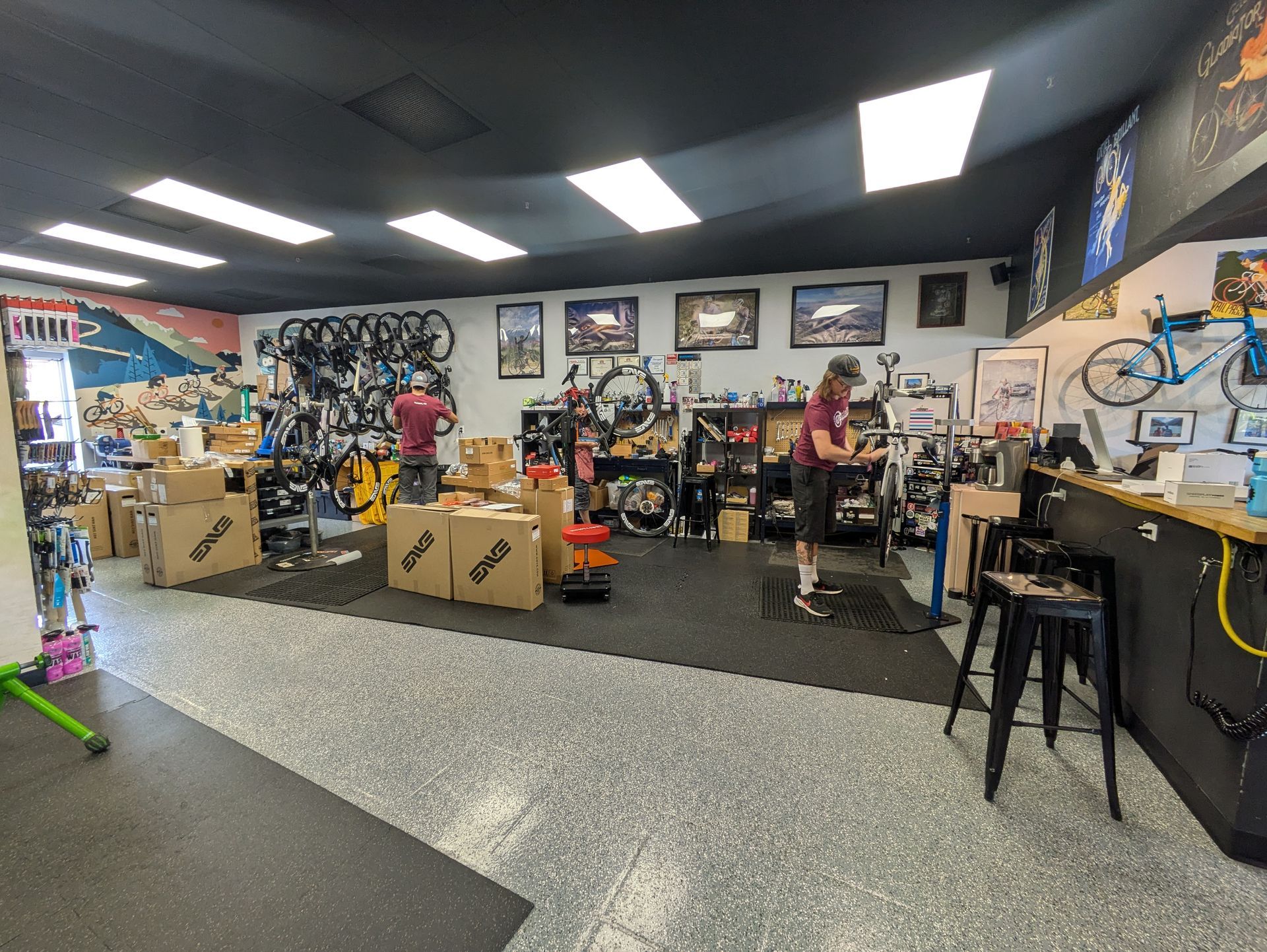 Bike shop interior with employees, bikes, and repair equipment. Boxes and merchandise on the floor.