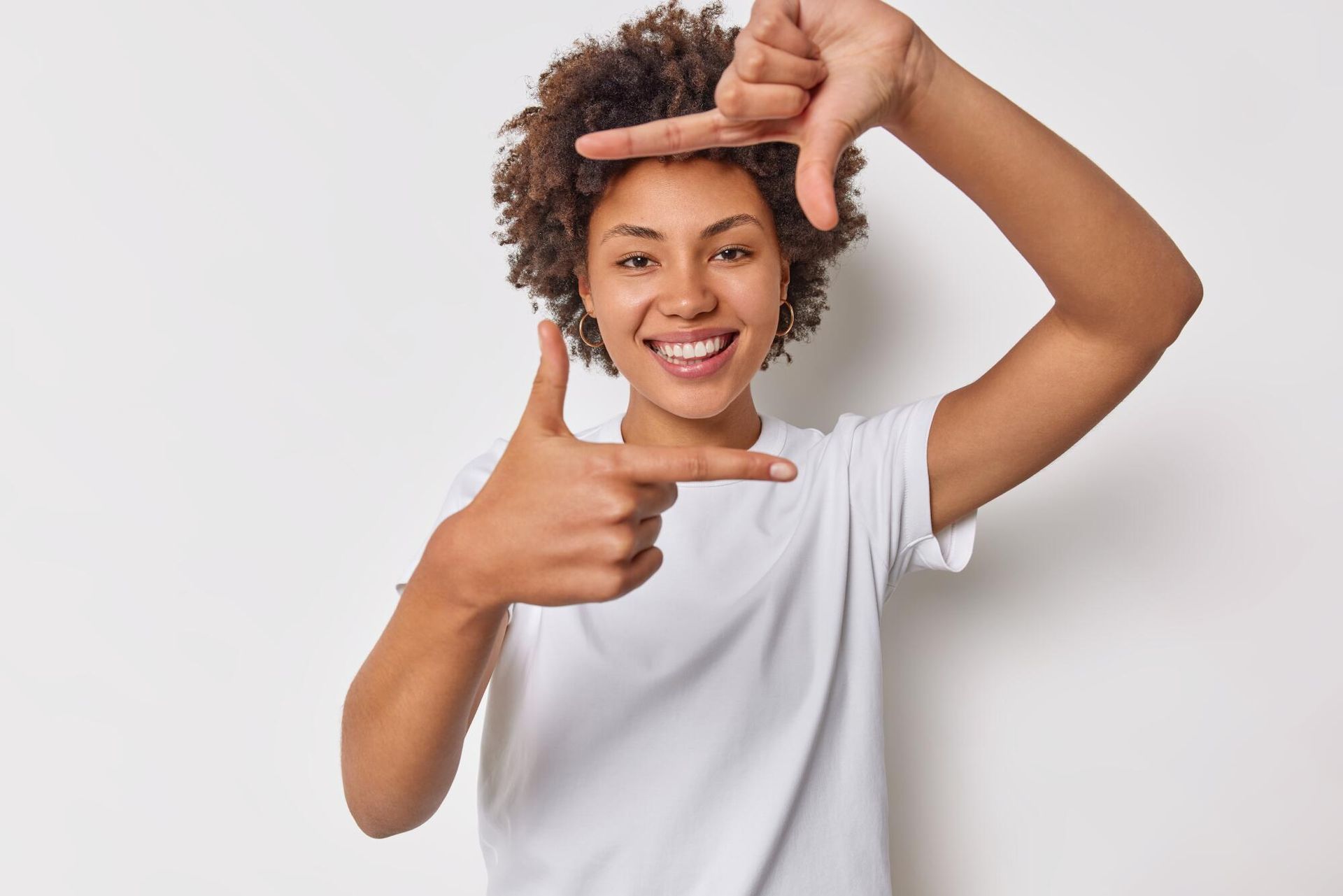 Smiling person in a white shirt making a frame gesture with their hands against a light background