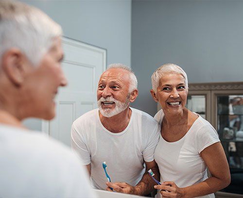 A man and a woman are brushing their teeth in front of a mirror.