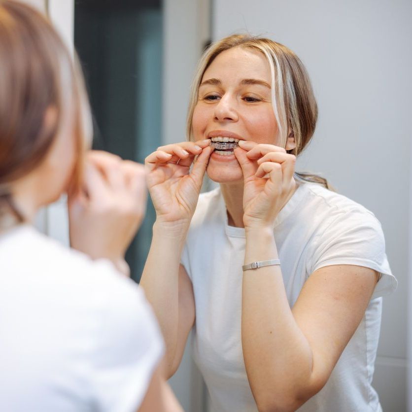 A woman is brushing her teeth in front of a mirror.