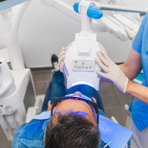 Person in dental chair receiving teeth whitening treatment under blue light.
