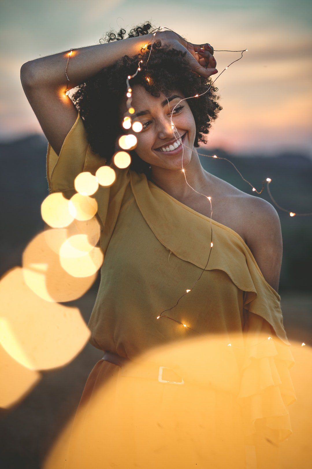 woman with dark curly hair and whitened teeth smiling and holding stringy lights