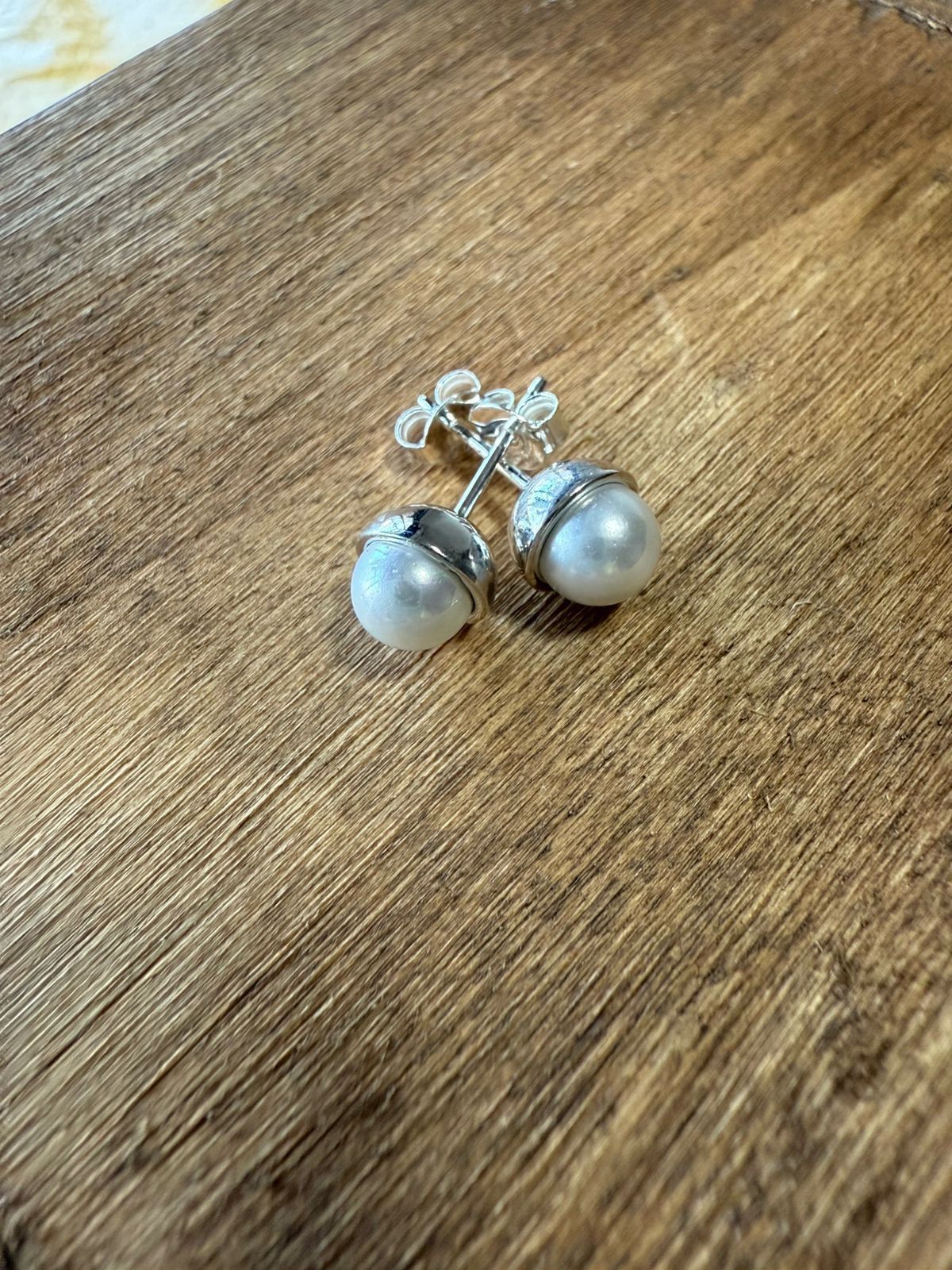 Pendientes de perlas con detalles plateados sobre superficie de madera.