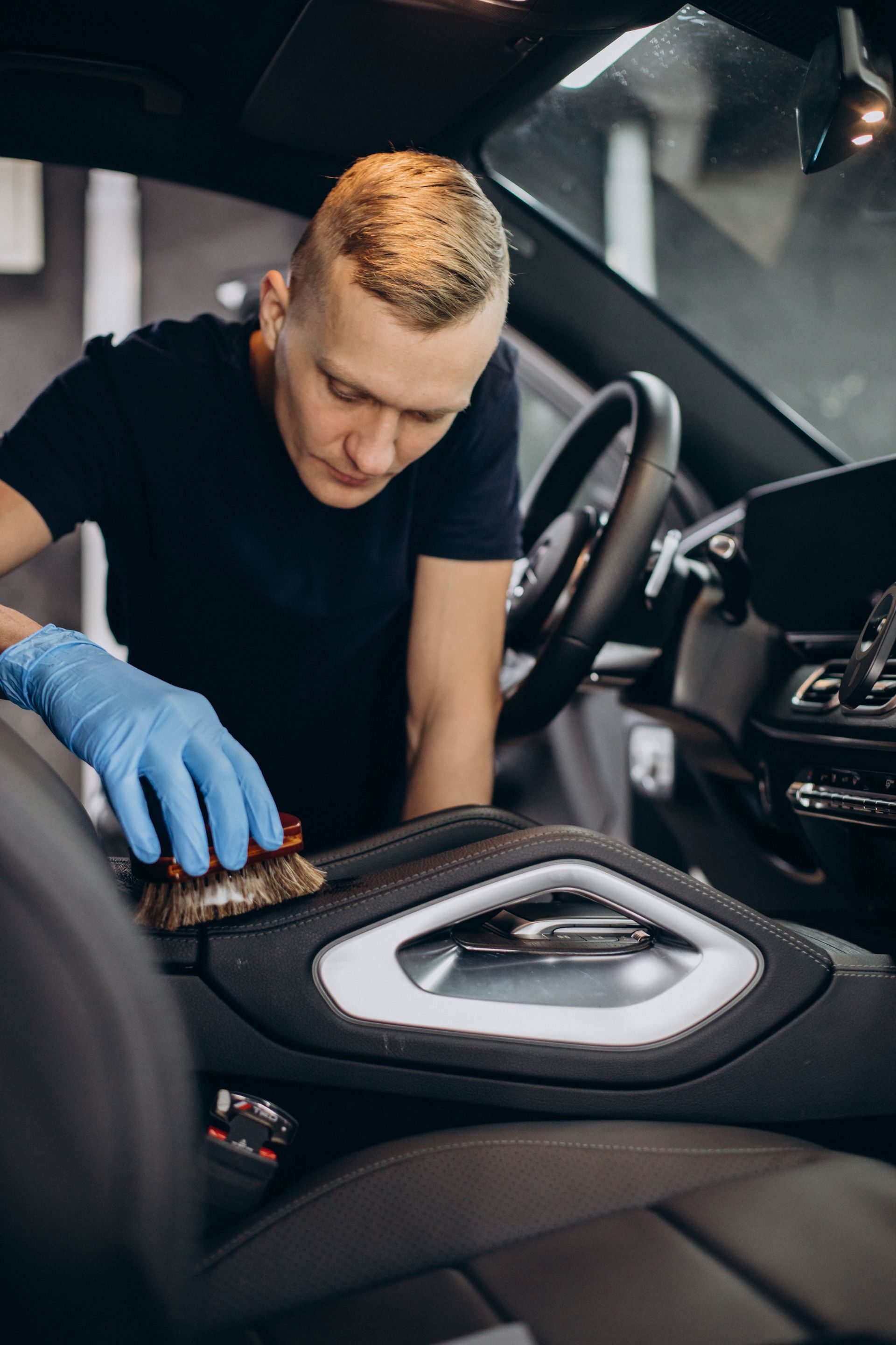Man in blue gloves cleaning a car's interior with a brush.