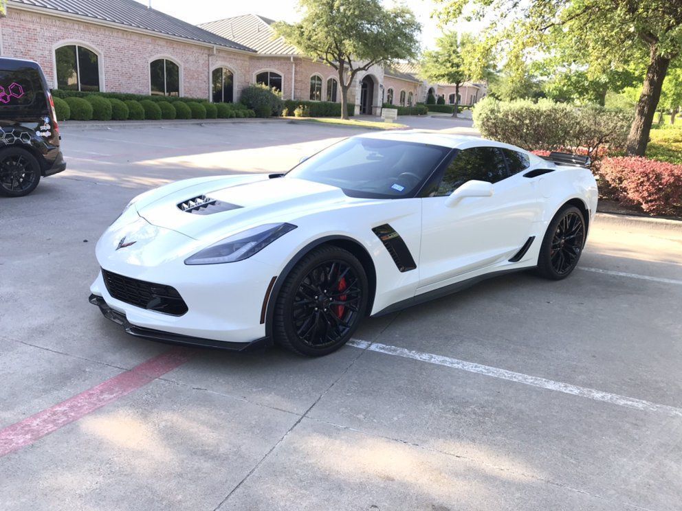 White Corvette sports car parked outside a building. Black wheels, red brake calipers.