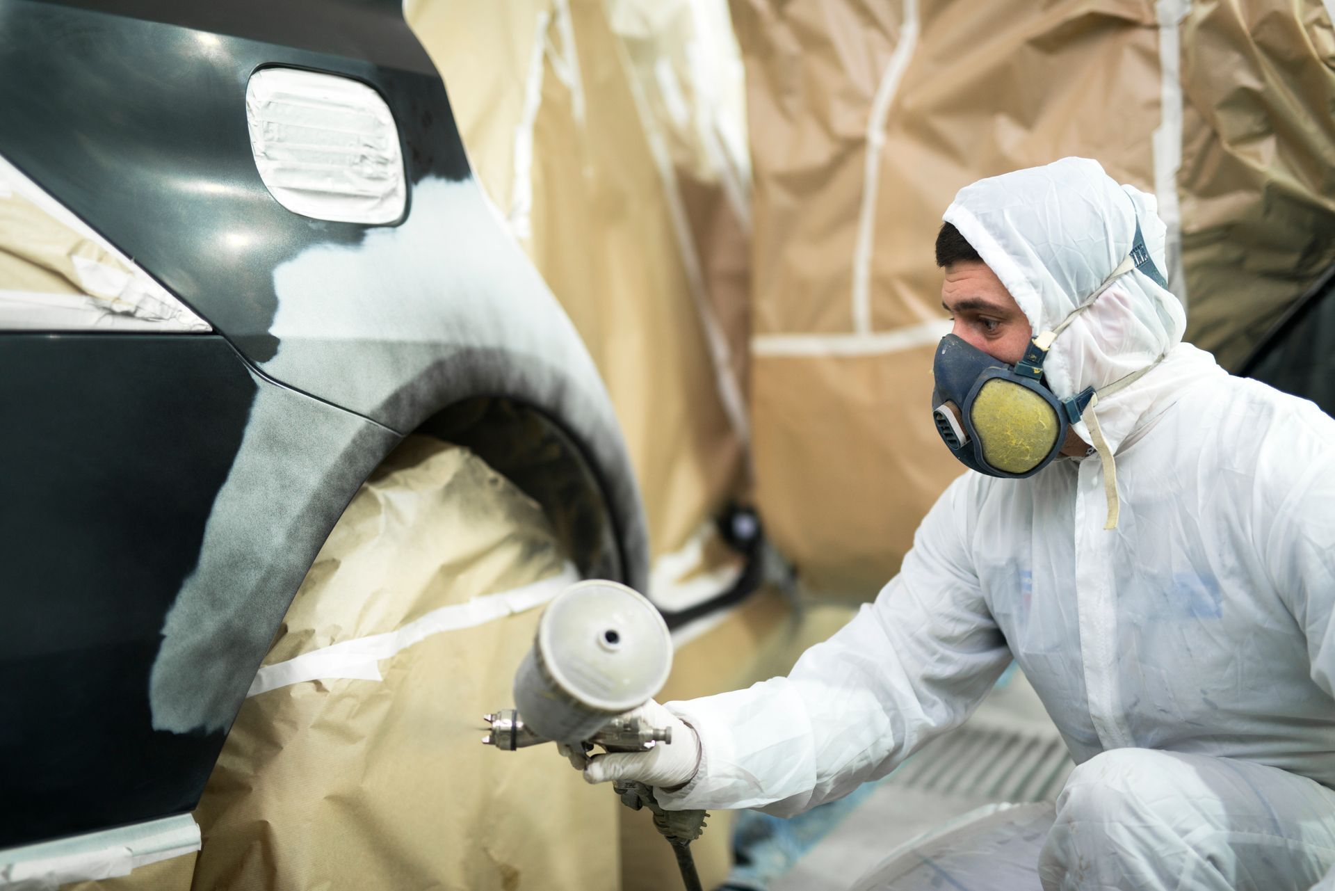 A person in protective gear spraying paint on a car in a workshop.