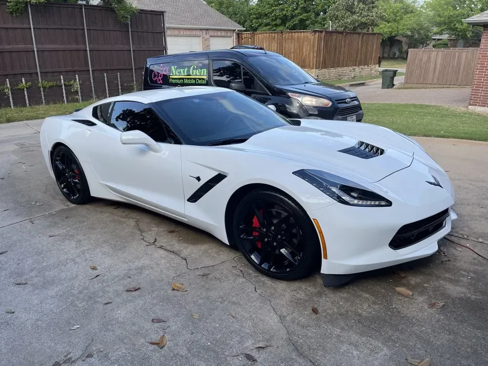 White sports car parked in a driveway beside a black van, front three-quarter view White sports car parked in a driveway beside a black van, front three-quarter view