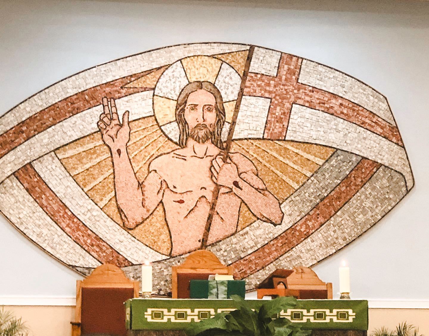Mosaic of a haloed figure raising a hand above a church altar, with a red cross in the background