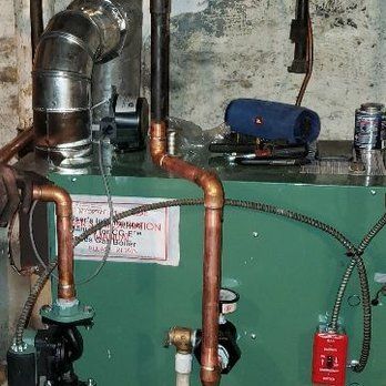 Green furnace with copper pipes, black pump, and red electrical box in a basement.