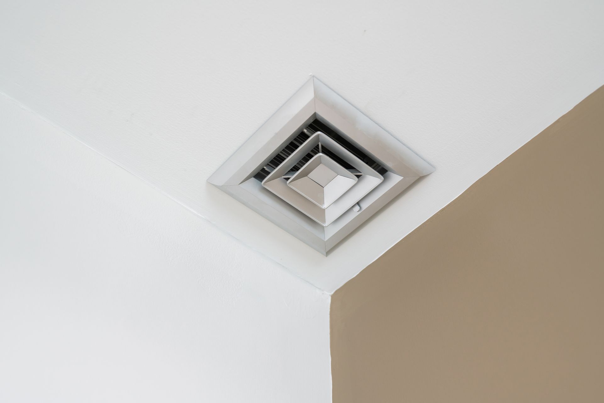 Silver air vent installed in the corner of a white and beige ceiling.