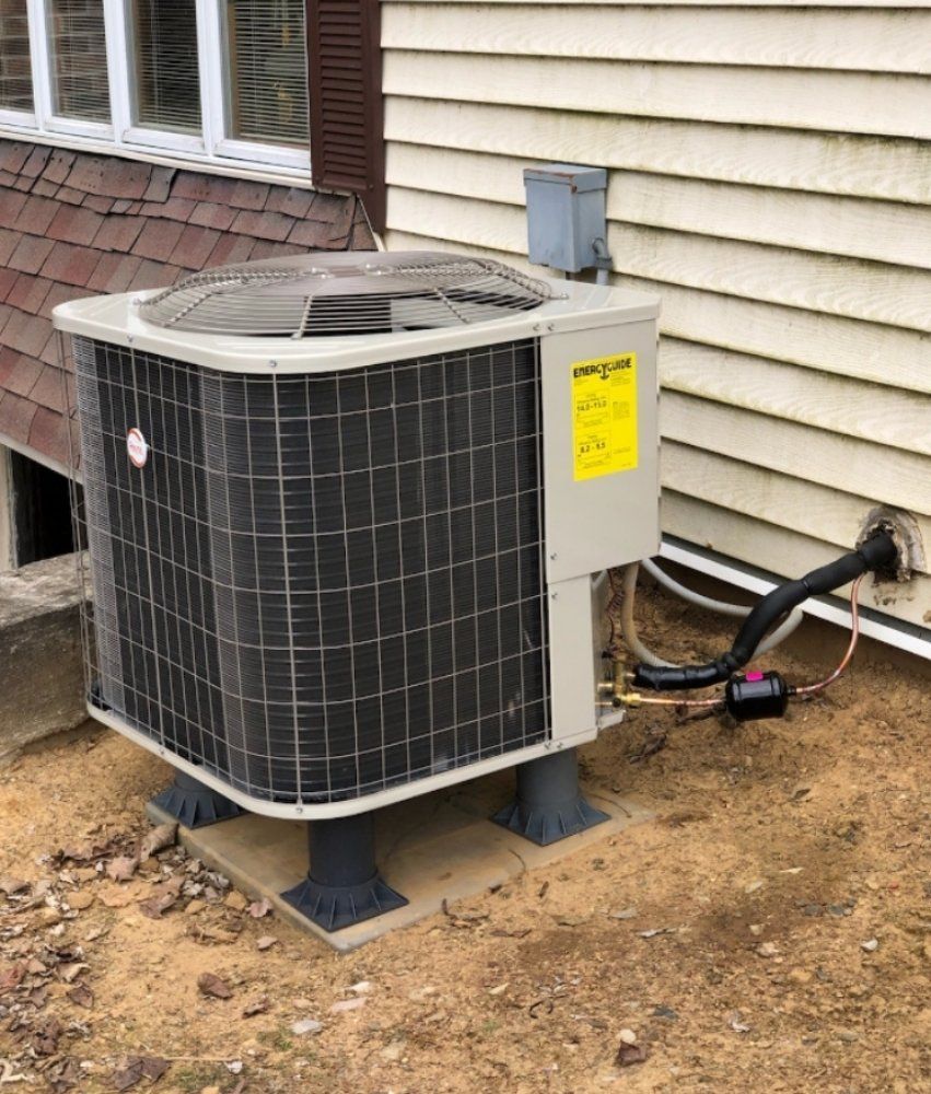 Outdoor Rheem air conditioning unit on a concrete base near a light beige house.