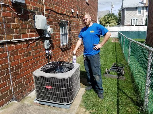Man standing next to an air conditioner unit outdoors on a grassy lawn.