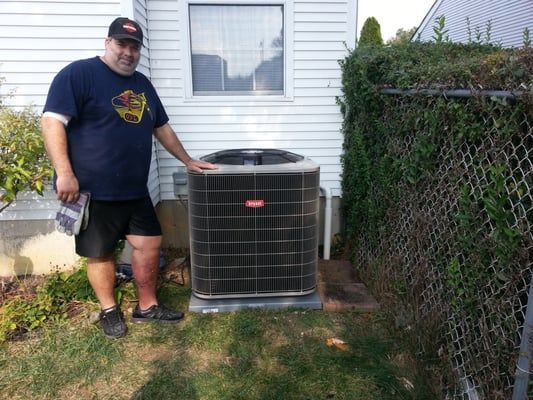 Man in shorts by a Bryant air conditioner unit. Backyard setting.