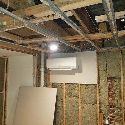 Renovation site with exposed beams and wall studs. Mini-split AC unit mounted on a drywall section.
