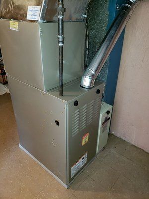 A tan furnace with a metal vent pipe and gas line in a basement setting.