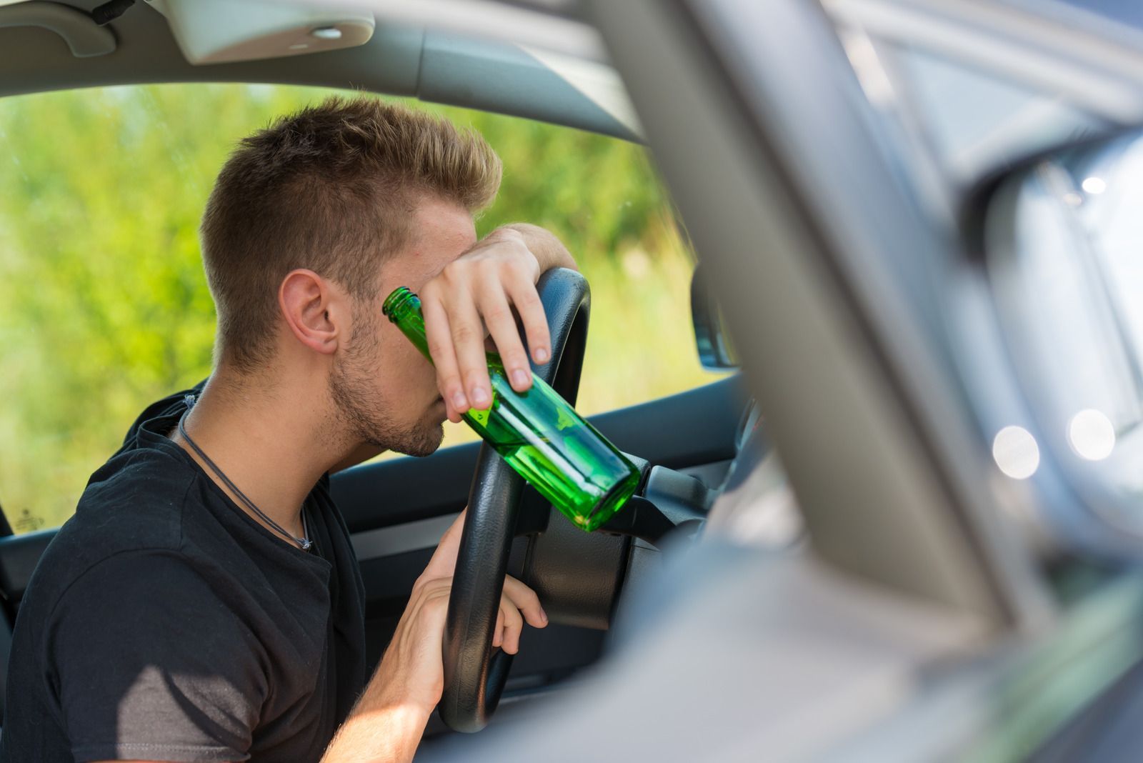 A man is drinking beer while driving a car.